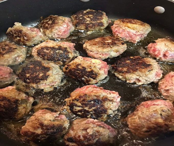 ground beef meatballs cooking in a cast iron skillet