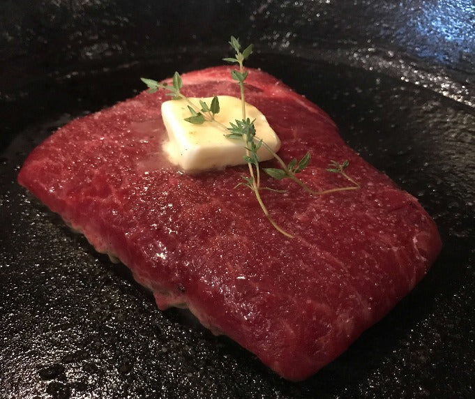 Flat iron steak cooking in a cast-iron skillet